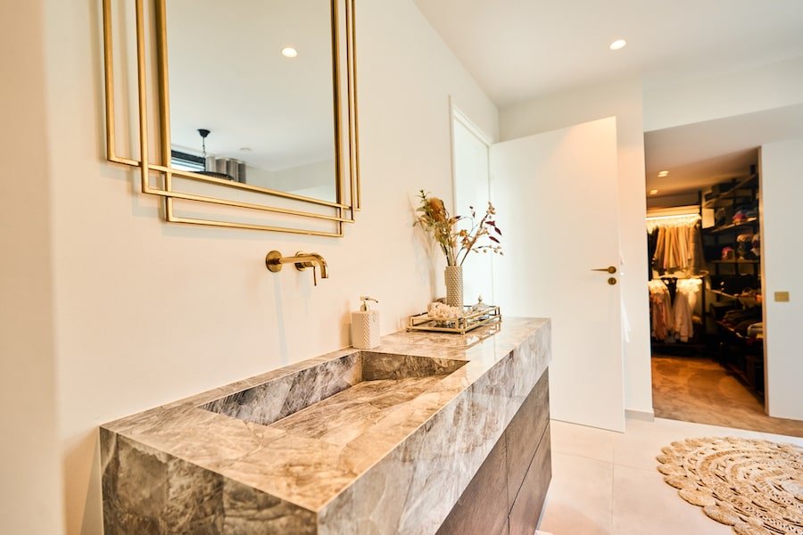 I det funkisbadeværelse er vasken indsat i en smukt marmorplade med et spejl omkranset af en elegant guldkant.